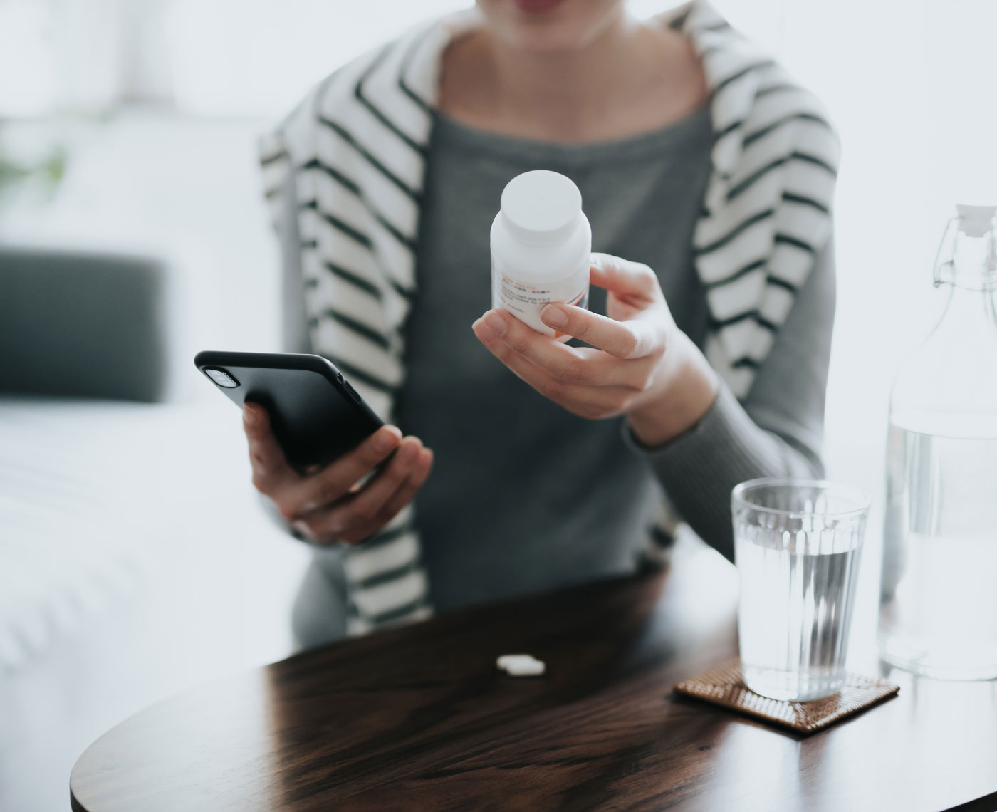 A woman holding a mobile phone and a bottle of pills