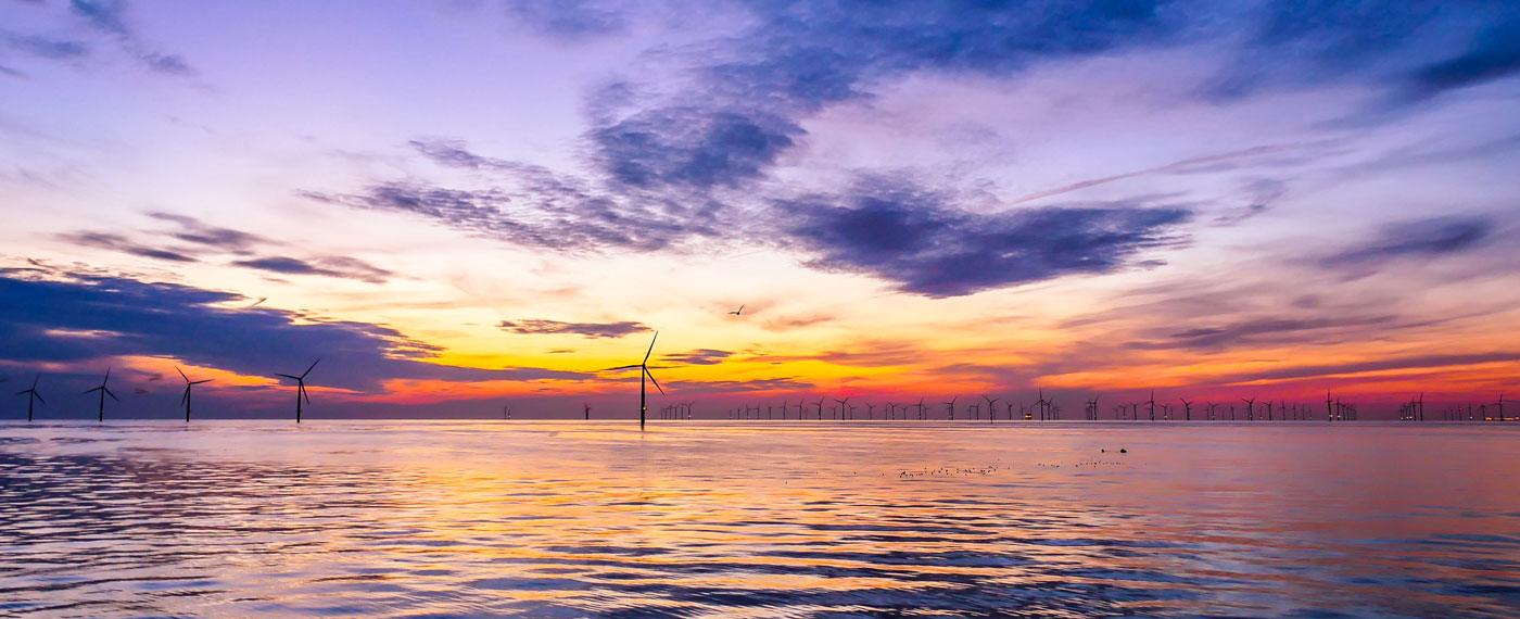 A wind farm out a sea with a sunset behind it