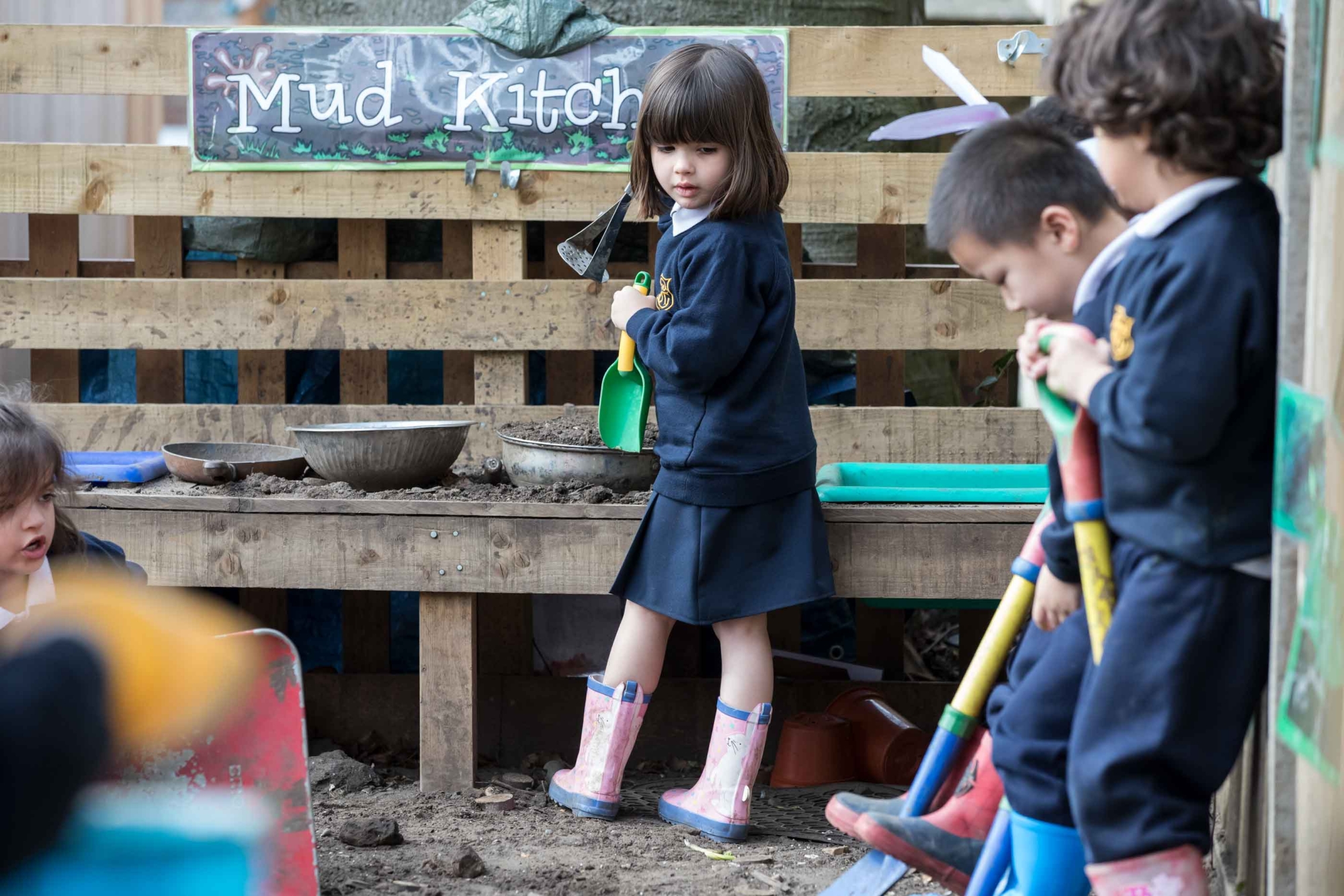 Young pupils play in the mud kitchen in the garden at their school