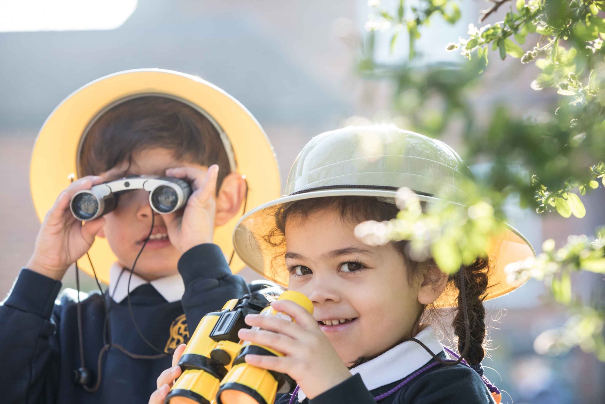 Two young pupils look through binoculars outside