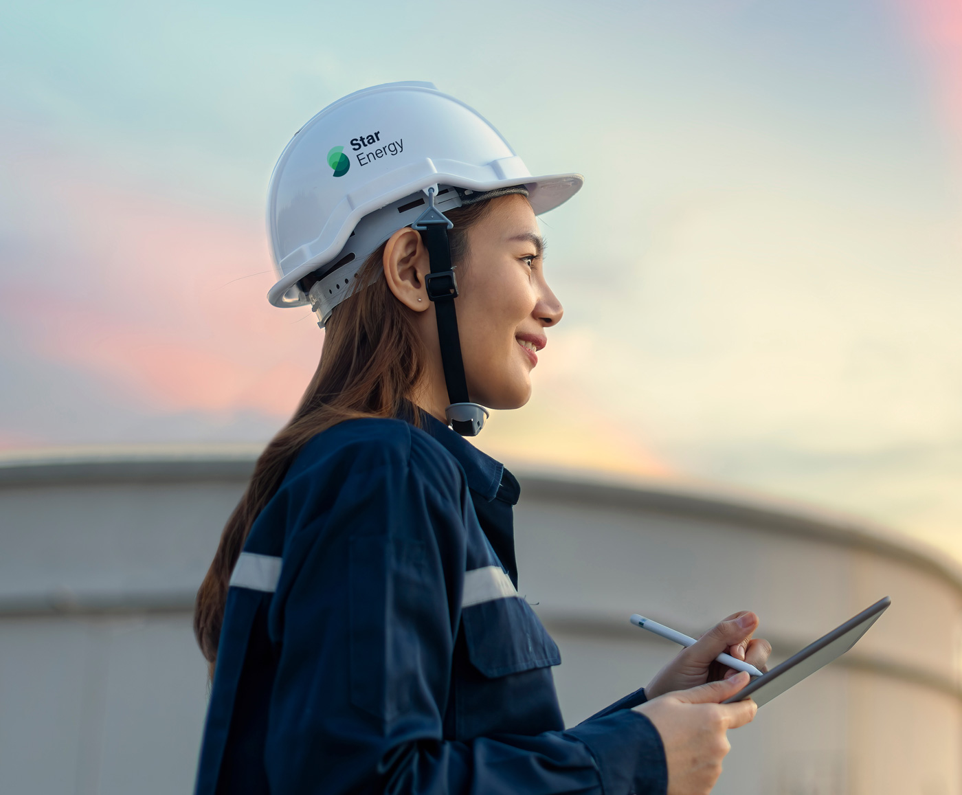 A woman standing outside wears blue coveralls and a hard hat showing the Star Energy brand, holding a clipboard